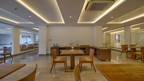 Un comedor moderno con mesas y sillas de madera, una isla central con un florero y un panel de vidrio que separa el comedor de la cocina.