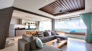 A modern living room with a grey sofa, wooden coffee table, and a view of the ocean. - Aqua Samui Villas (Koh Samui)