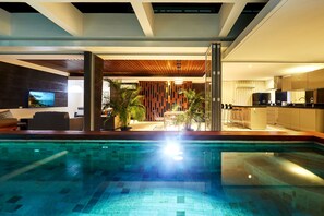 Un área de piscina interior moderna con vista despejada al espacio de estar contiguo, que incluye un rincón de descanso y una cocina.