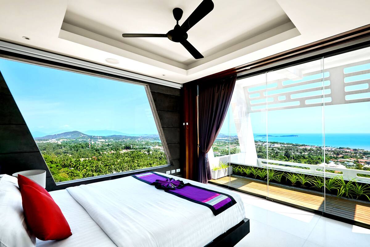 Ein modernes Schlafzimmer mit einem großen Bett, einem Deckenventilator und Blick auf eine Küstenlandschaft.