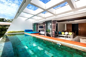 A modern house with a glass-enclosed swimming pool, a blue sofa, and a dining area with a table and chairs. - Aqua Samui Villas (Koh Samui)