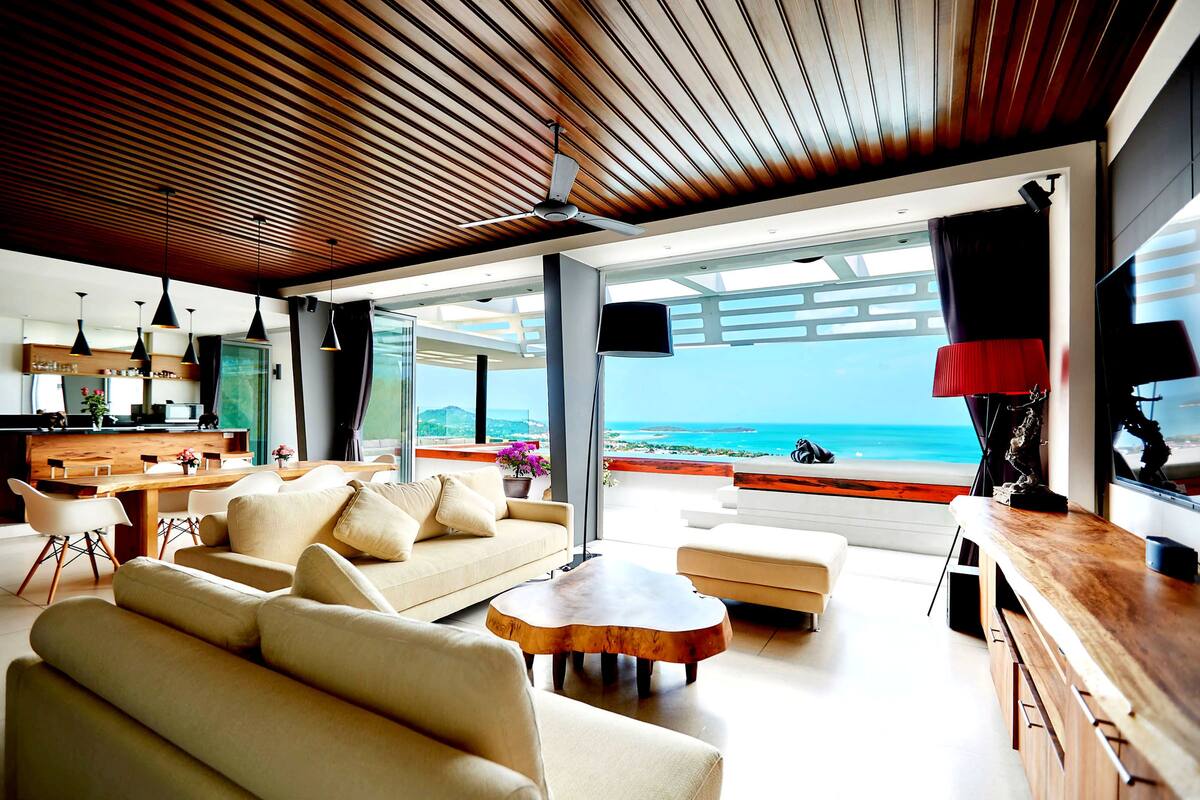 Ein modernes Wohnzimmer mit Holzboden, großen Fenstern und Blick auf den Strand.