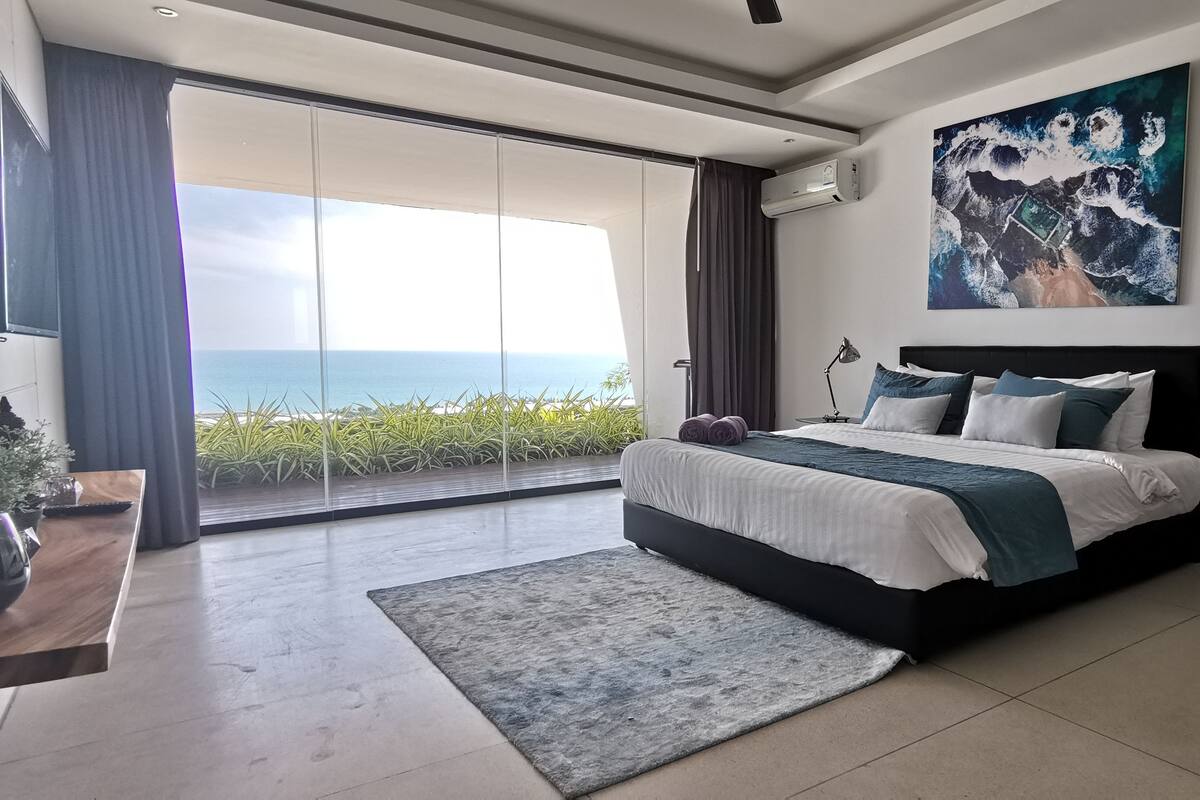 Ein modernes Schlafzimmer mit einem großen Bett, Meerblick und einem Bild an der Wand.
