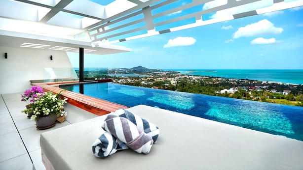 A modern infinity pool with a clear view of the ocean and a cityscape. - Aqua Samui Villas (Koh Samui)