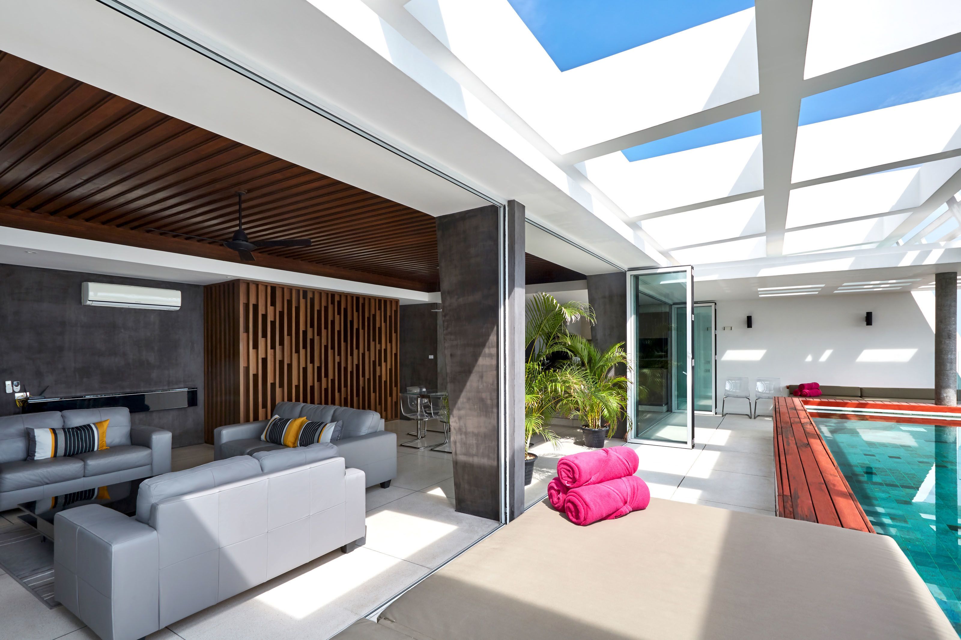 A modern living room with a pool, grey sofas, and a wooden ceiling.