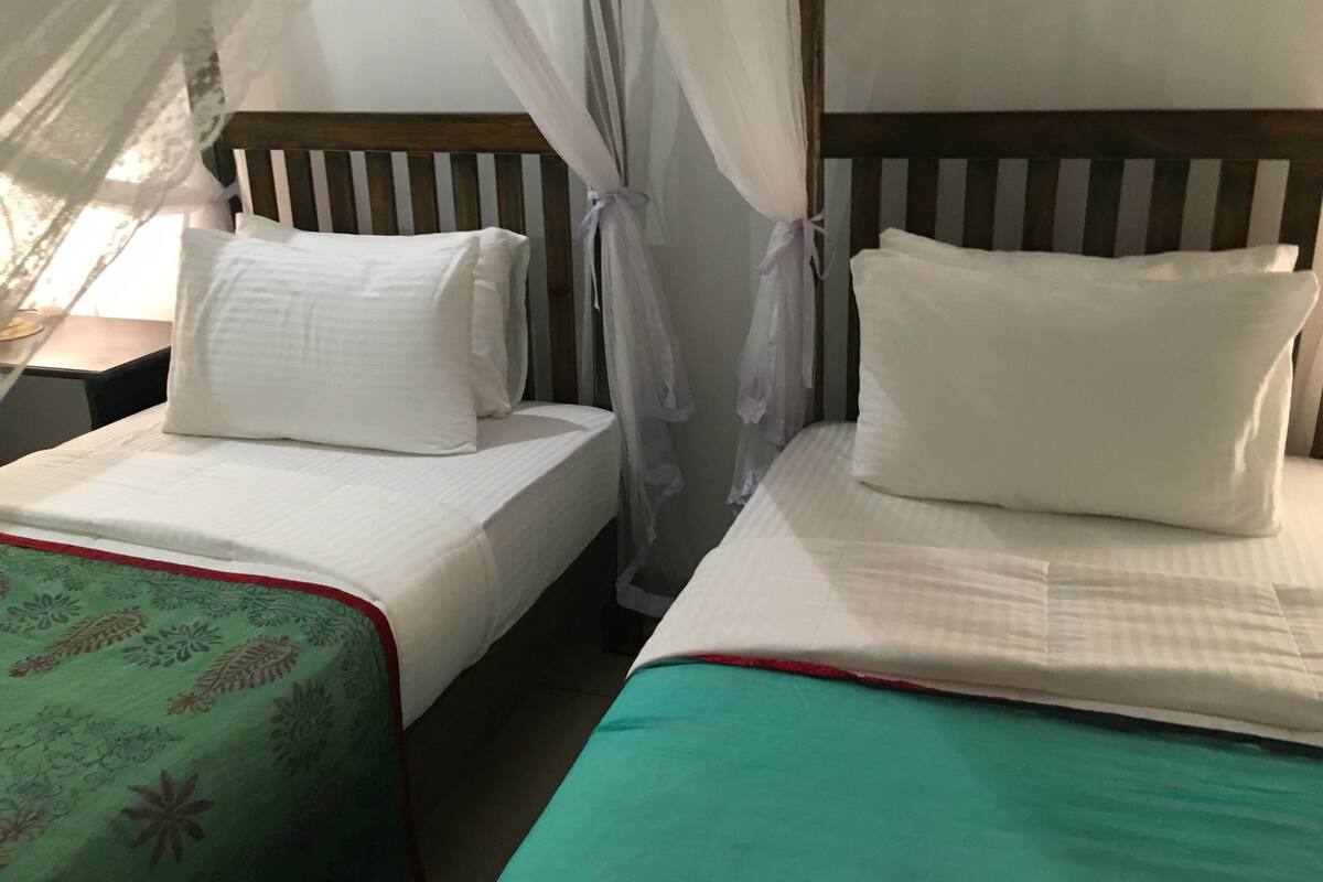 Een kamer met twee bedden, elk voorzien van witte lakens en een houten hoofdbord.