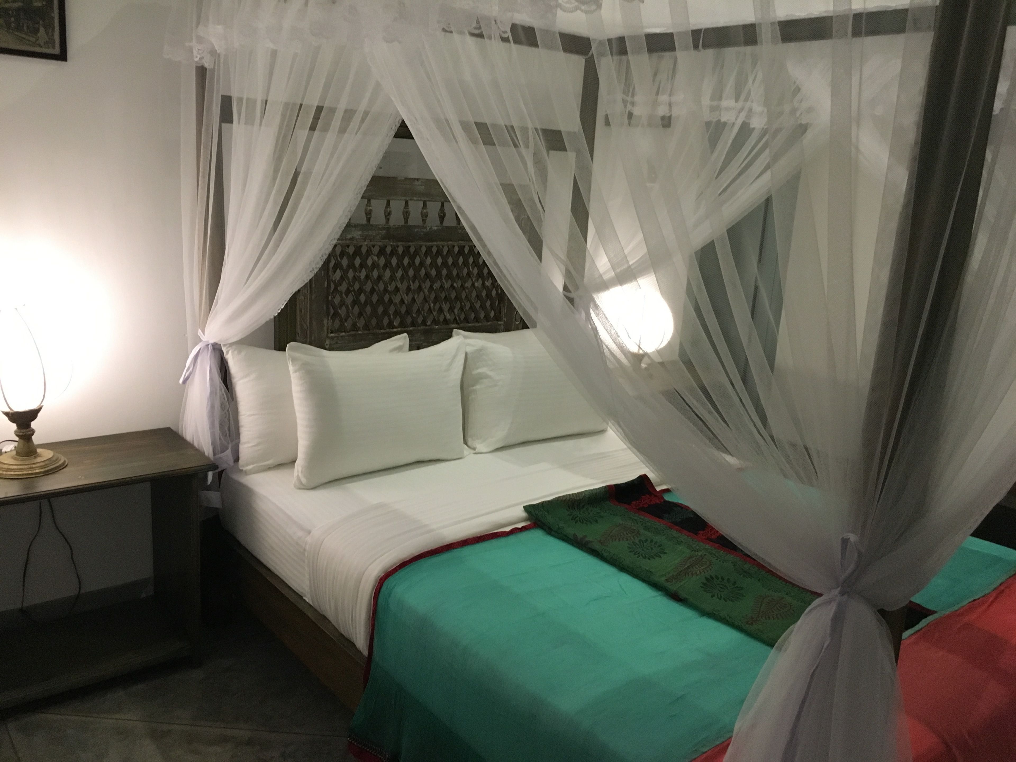 A bed with a canopy, a bedside table with a lamp, and a green bedspread.