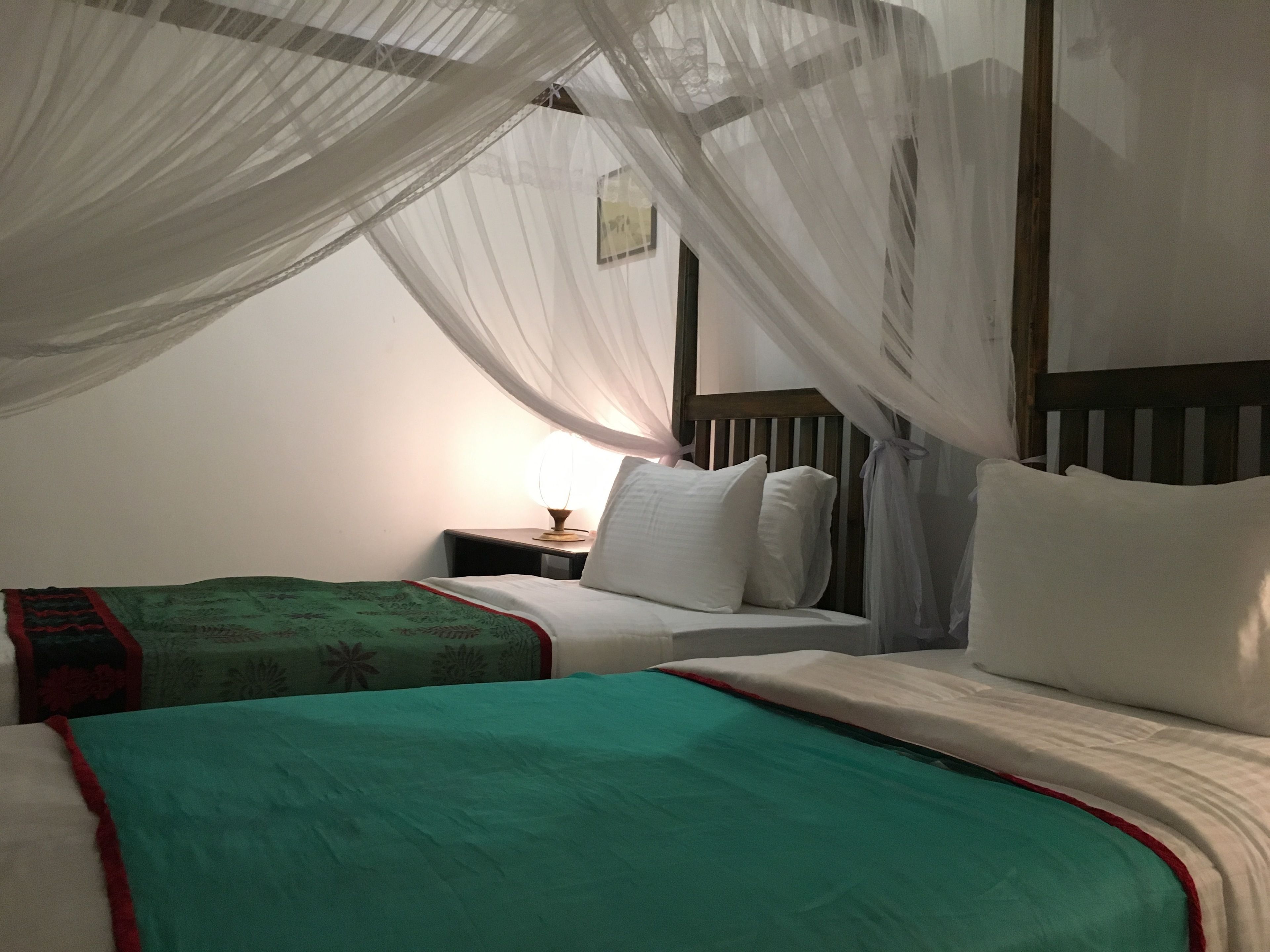 Un dormitorio con cama, mesita de noche, lámpara y mosquitera.