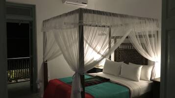 A four-poster bed with white bedding and a red blanket, an air conditioning unit above, and a balcony with a metal railing.