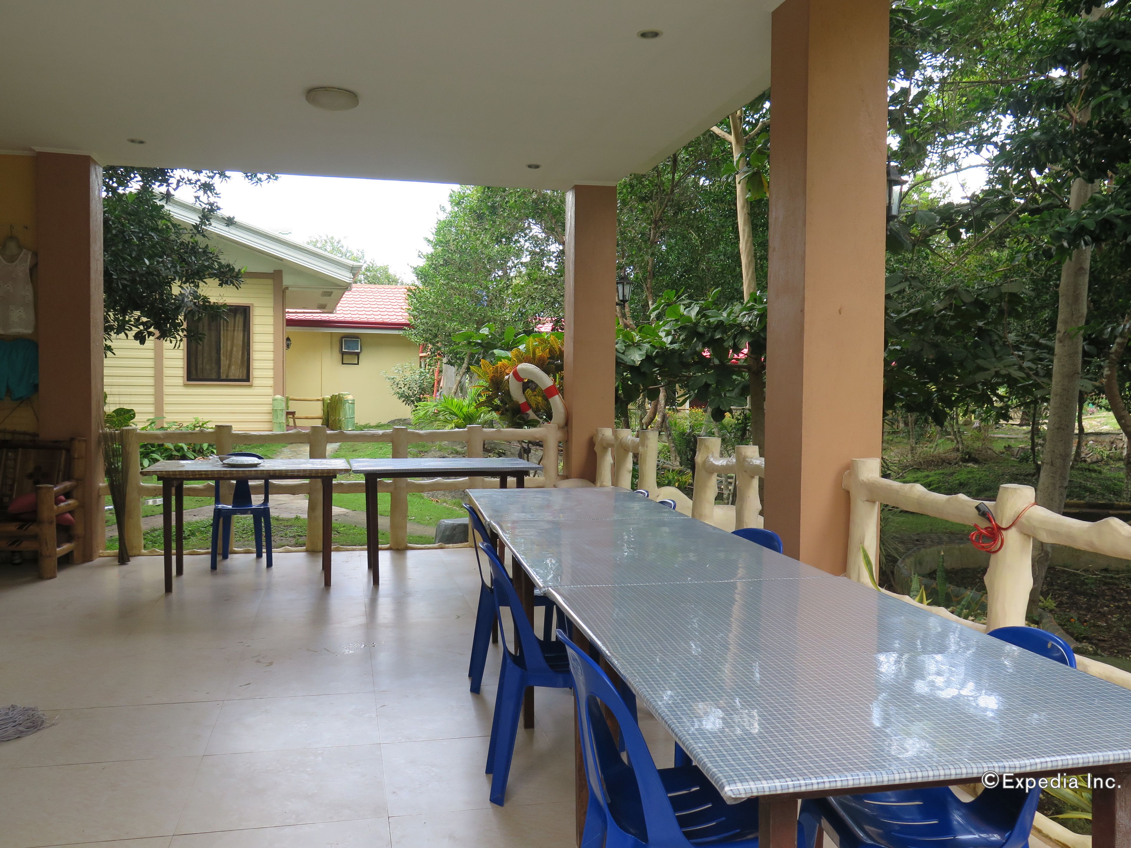 An outdoor patio with a long table and blue chairs, surrounded by a wooden fence and greenery.