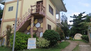 A building with a unique staircase design, a signboard, and surrounding greenery.