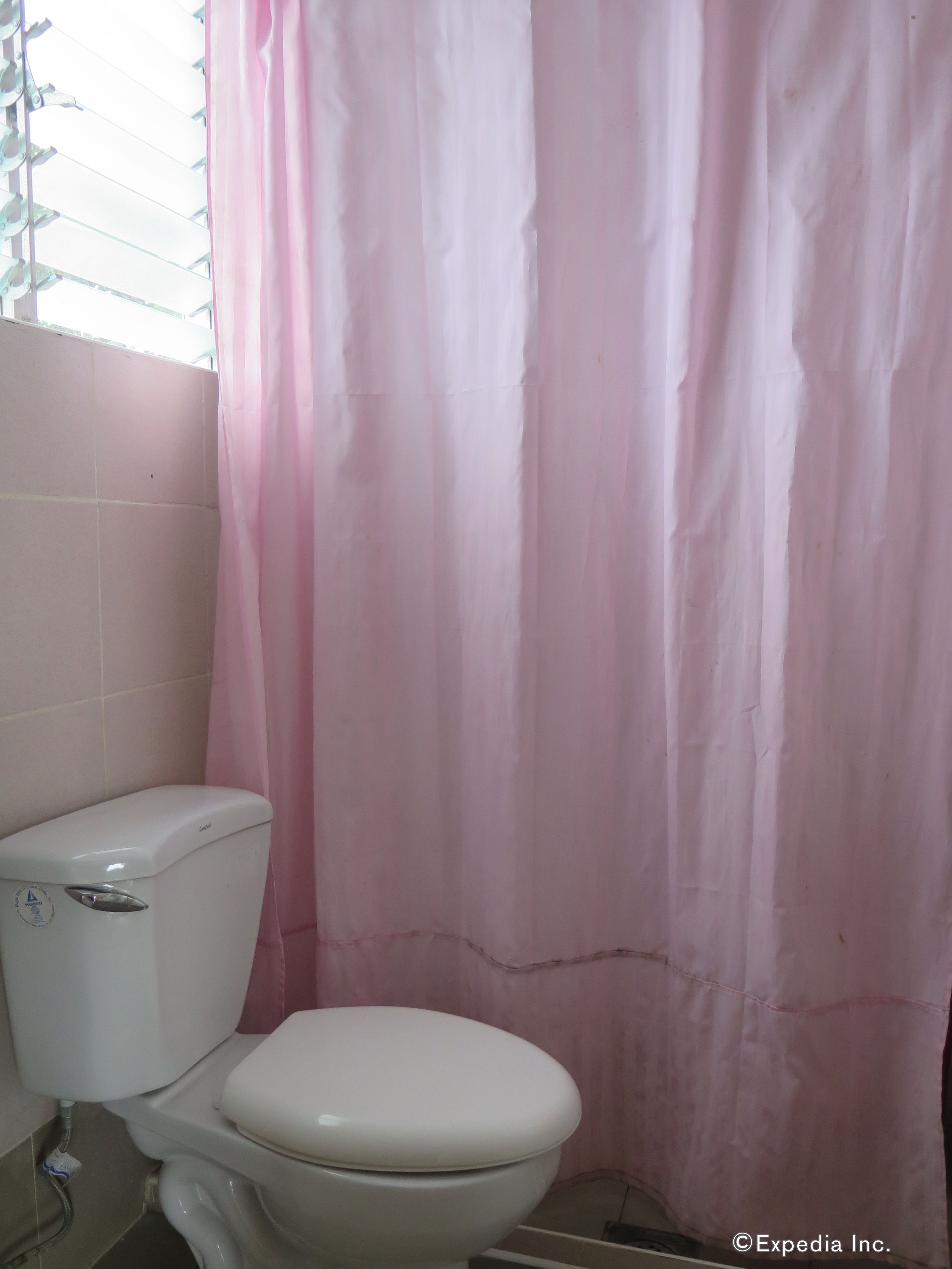 Ett badrum med en vit toalett, ett rosa duschdraperi och kaklade väggar.