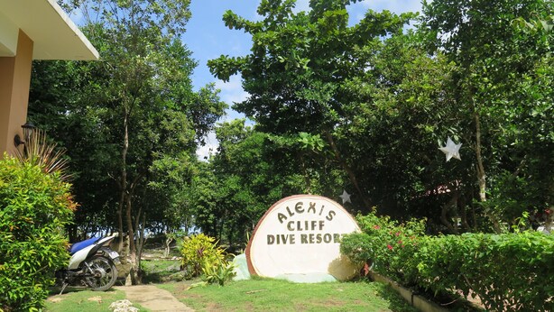 A sign for 'Alexis Cliff Dive Resort' surrounded by lush greenery and a parked motorcycle.
