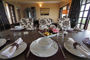 A dining table set for four with floral-patterned chairs, a bowl of fruit, and a vase of flowers. - Deacra Villas By Sol Resorts (Vilanculos)