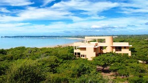 A modern building with a flat roof and large windows, surrounded by lush greenery and overlooking a beach. - Deacra Villas By Sol Resorts (Vilanculos)