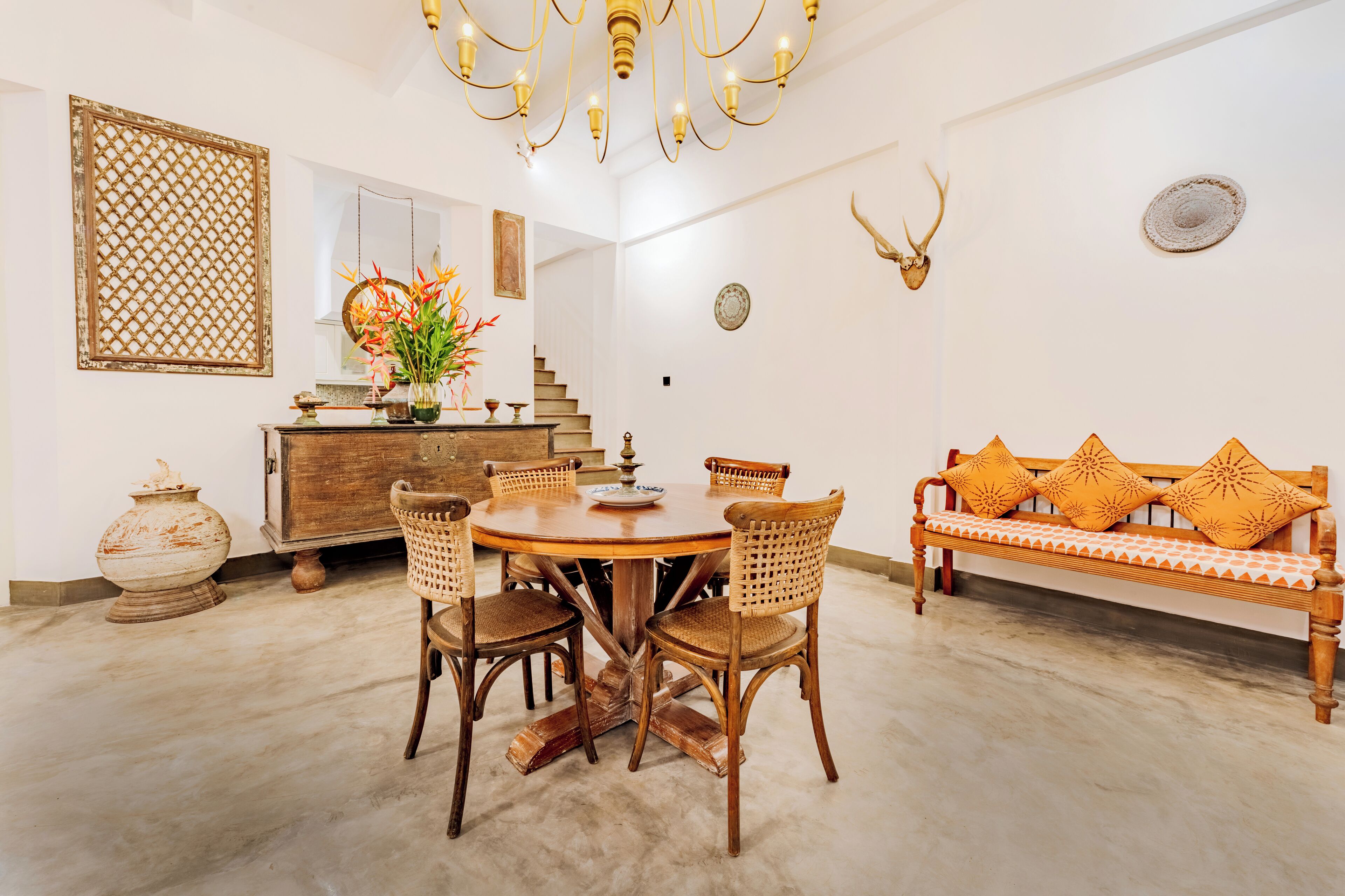 Un comedor con una mesa redonda de madera, sillas de mimbre y un banco de madera con cojines estampados.