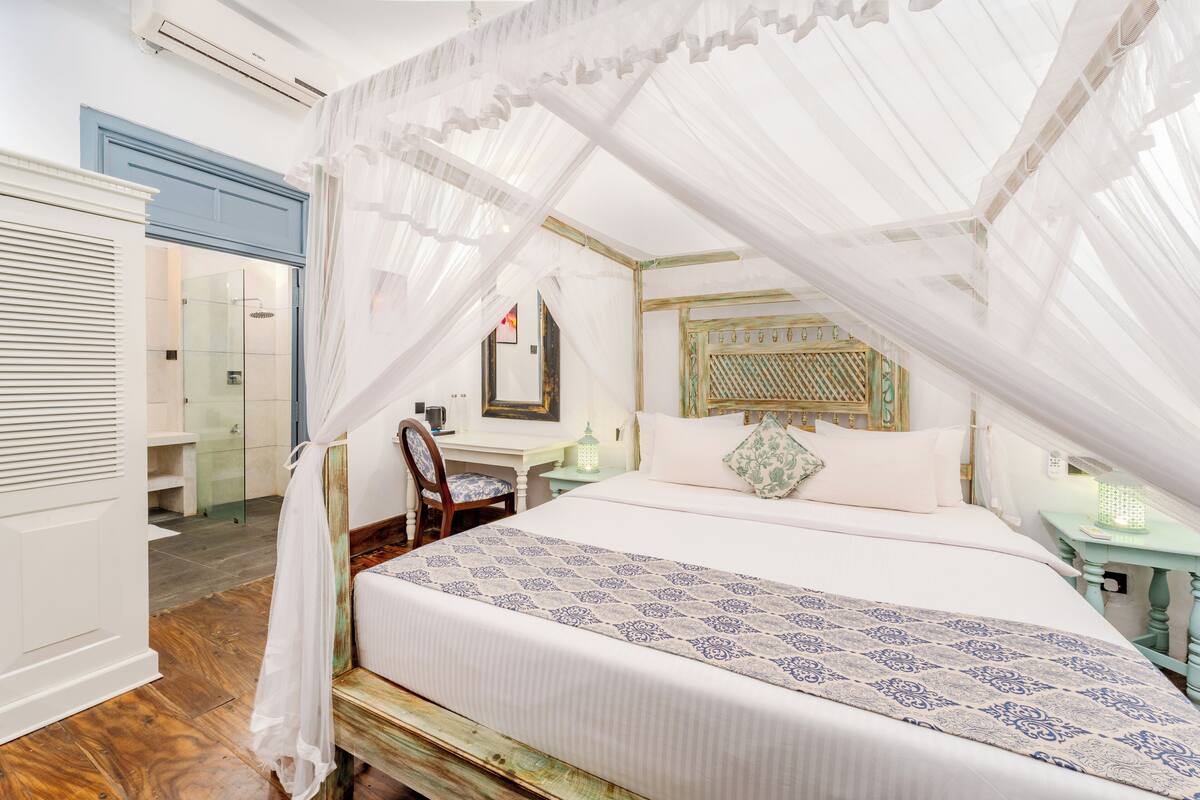 Une chambre à coucher avec un lit à baldaquin, un banc en bois, un bureau et une chaise.