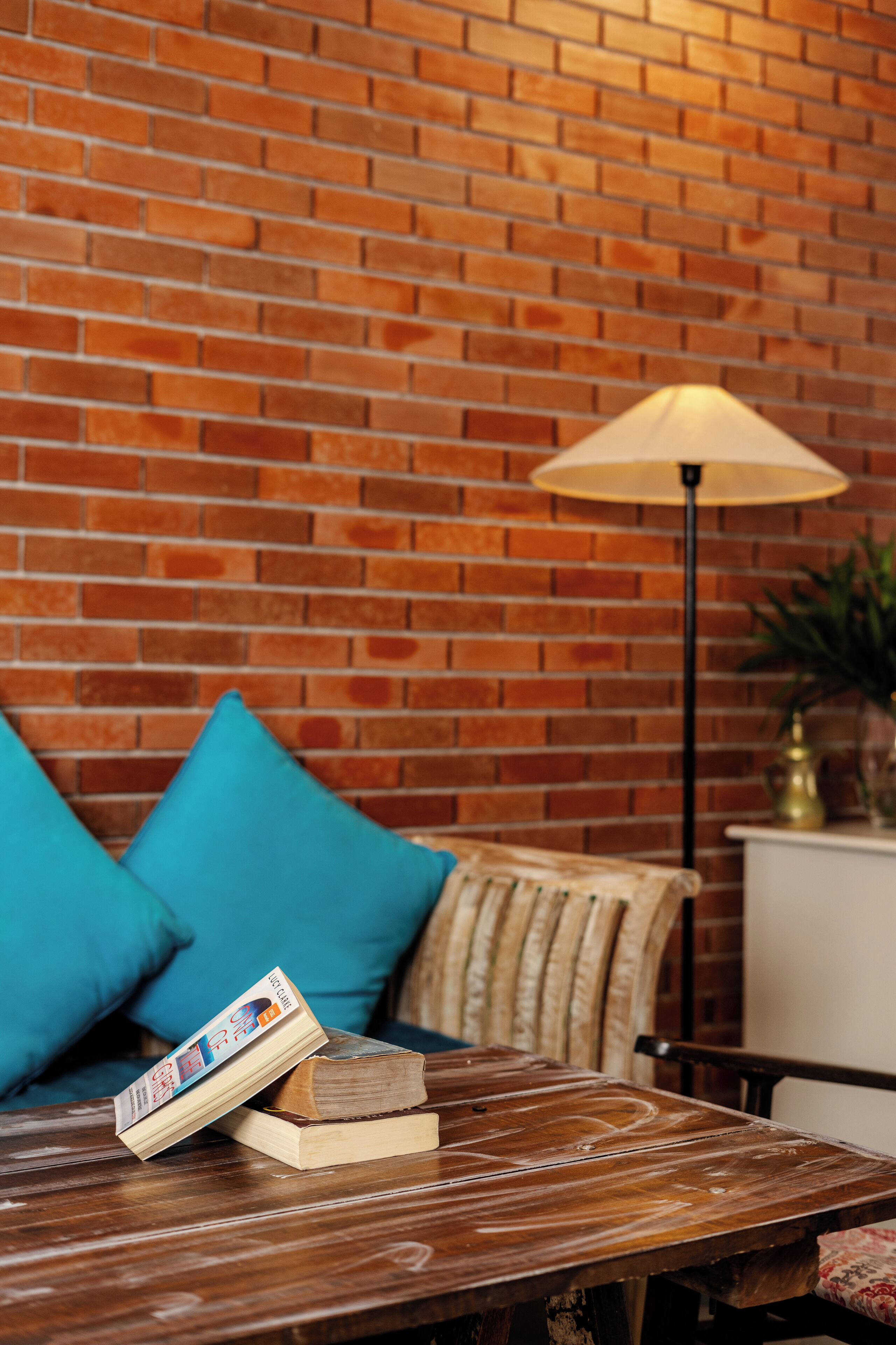 A wooden table with books and a lamp against a brick wall.