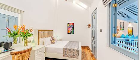 A bedroom with a bed, a desk, a chair, a ceiling fan, and a view of an outdoor balcony.