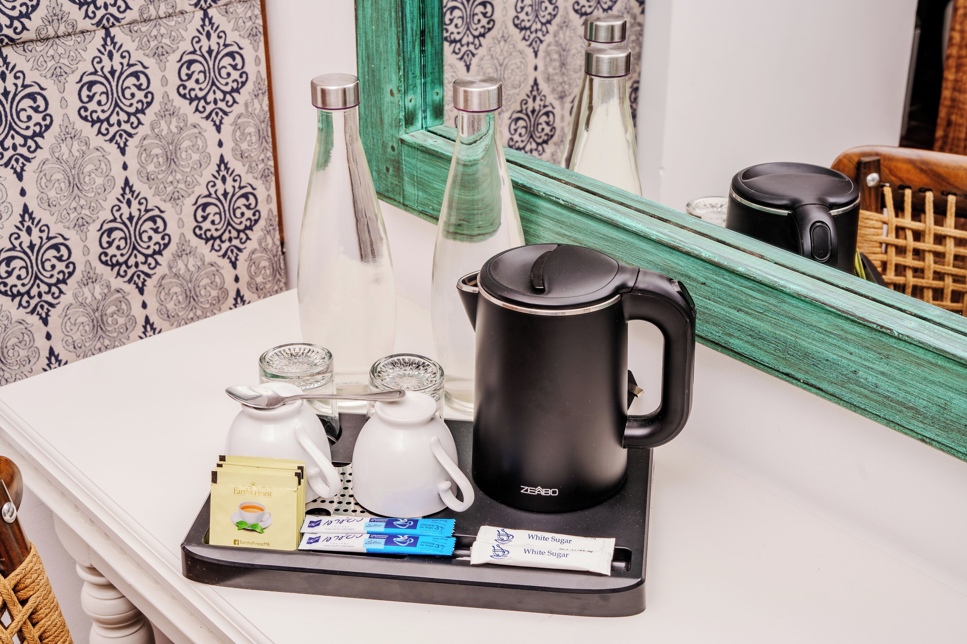 A tray with a black coffee maker, a white teapot, two glass cups, and packets of tea and sugar on a white countertop.