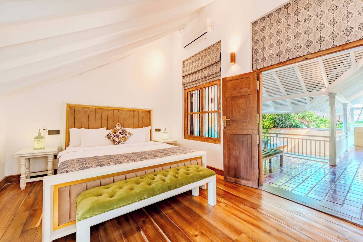 Une chambre à coucher avec un lit en bois, un banc vert, une table de chevet et une fenêtre ornée de rideaux à motifs.
