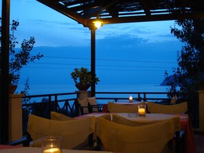 A restaurant with outdoor seating overlooking a body of water, featuring tables with candles and potted plants. - Mounda Beach Hotel (Kefalonia)