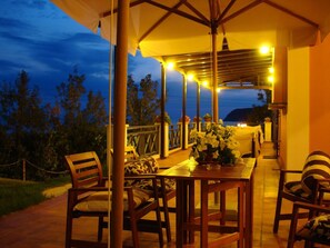 An outdoor patio with wooden furniture and a table, surrounded by a covered area with string lights. - Mounda Beach Hotel (Kefalonia)