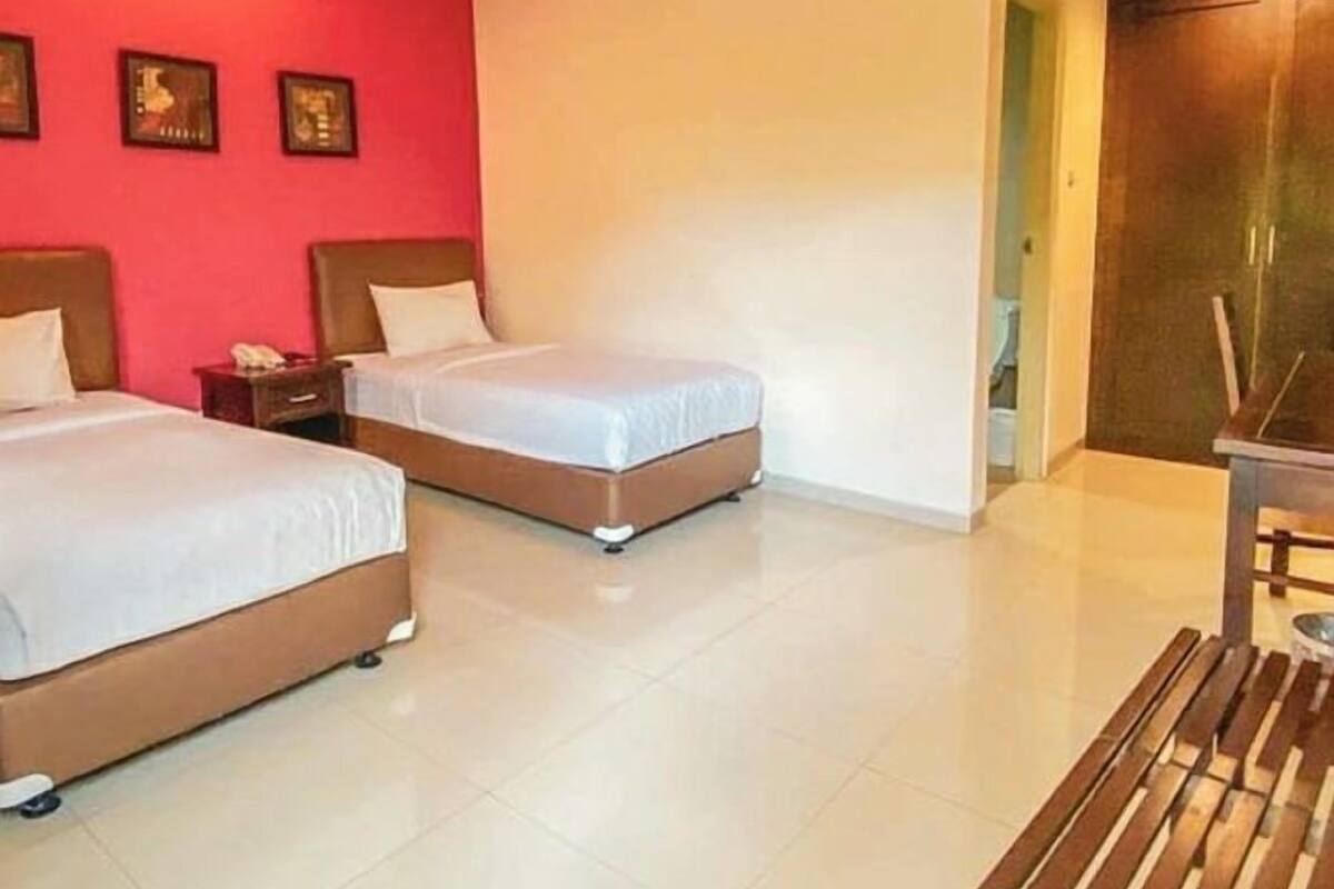 A hotel room with two beds, a wooden bench, and a red accent wall.