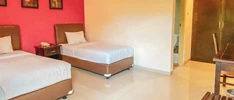 A hotel room with two beds, a wooden bench, and a red accent wall.