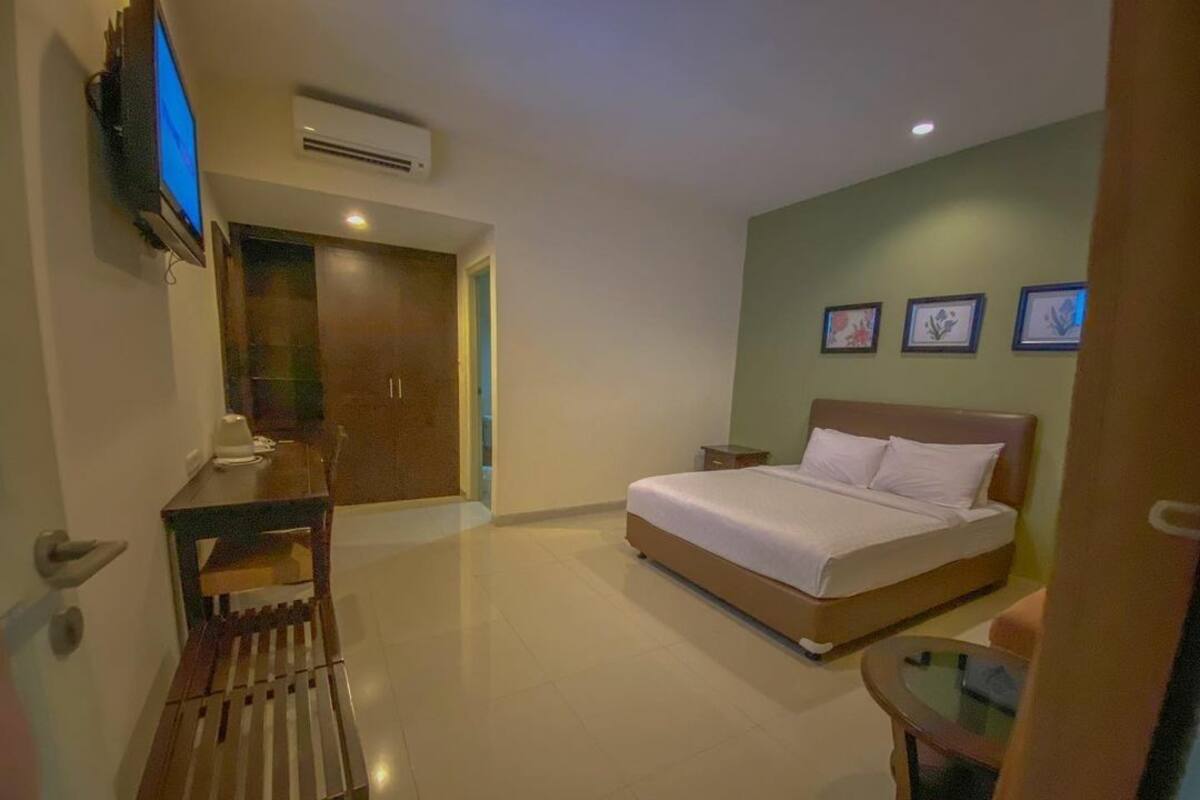 A bedroom with a bed, a desk, a chair, and a TV mounted on the wall.