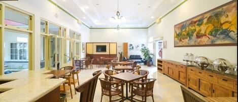 Un comedor amplio con mesas y sillas de madera, un cuadro grande en la pared y un mostrador de buffet con diversos platos.