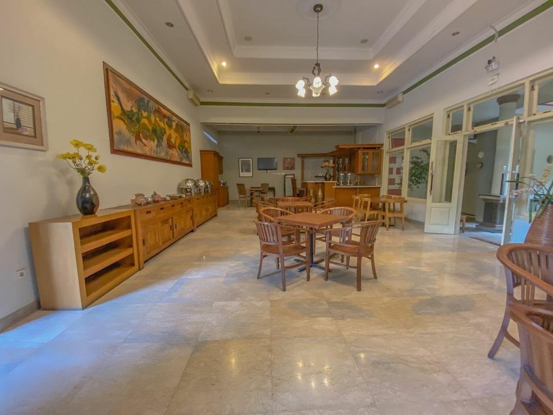 Un'ampia sala da pranzo con tavolo e sedie in legno, un grande quadro appeso al muro e una cucina sullo sfondo.