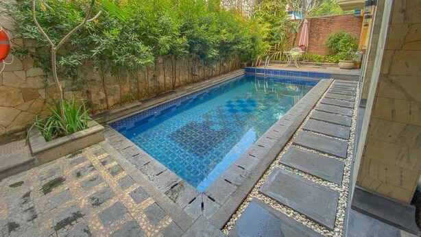Una piscina con paredes de piedra y suelo de baldosas, rodeada de vegetación y un muro de piedra.