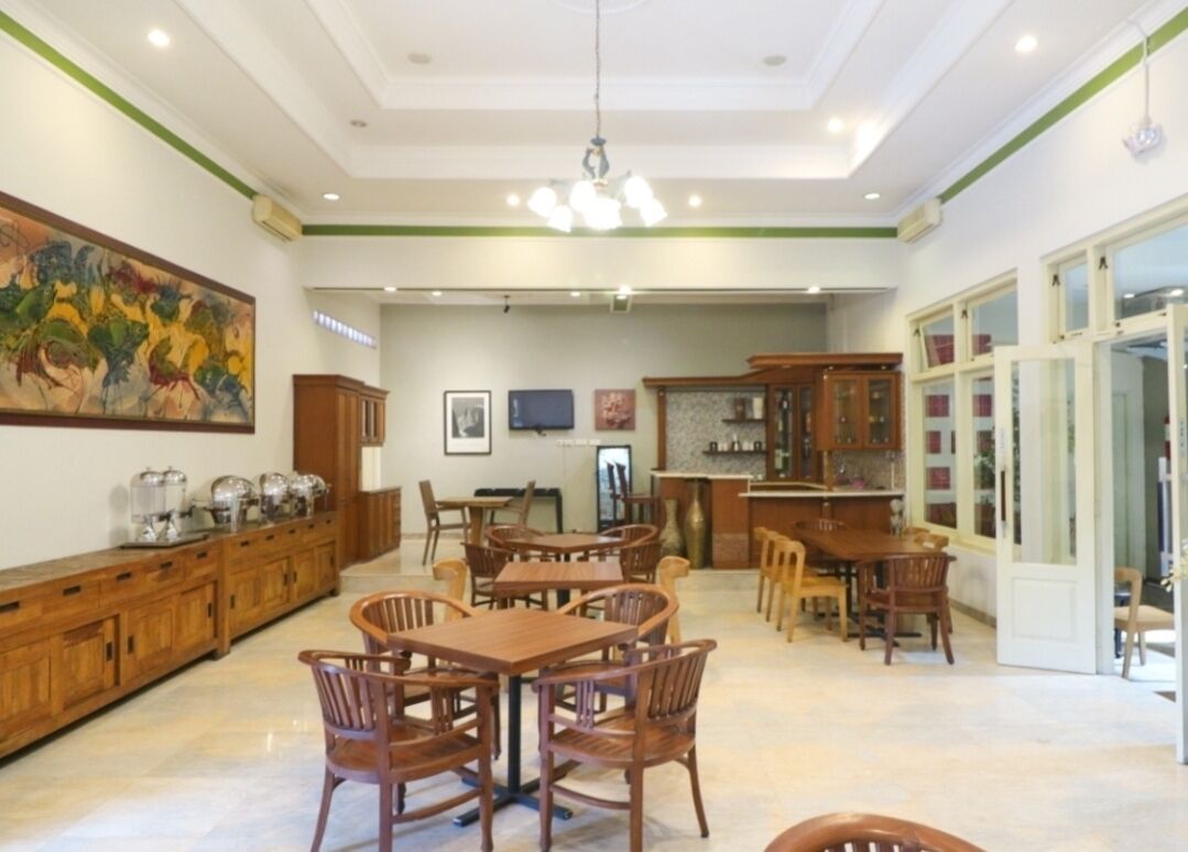 Een ruime eethoek met houten tafels en stoelen, een groot schilderij aan de muur, en een bar met houten kasten.