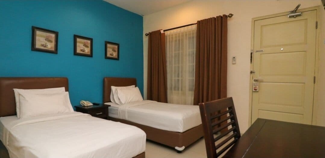 A hotel room with two beds, a wooden table, a chair, a nightstand, and a door.