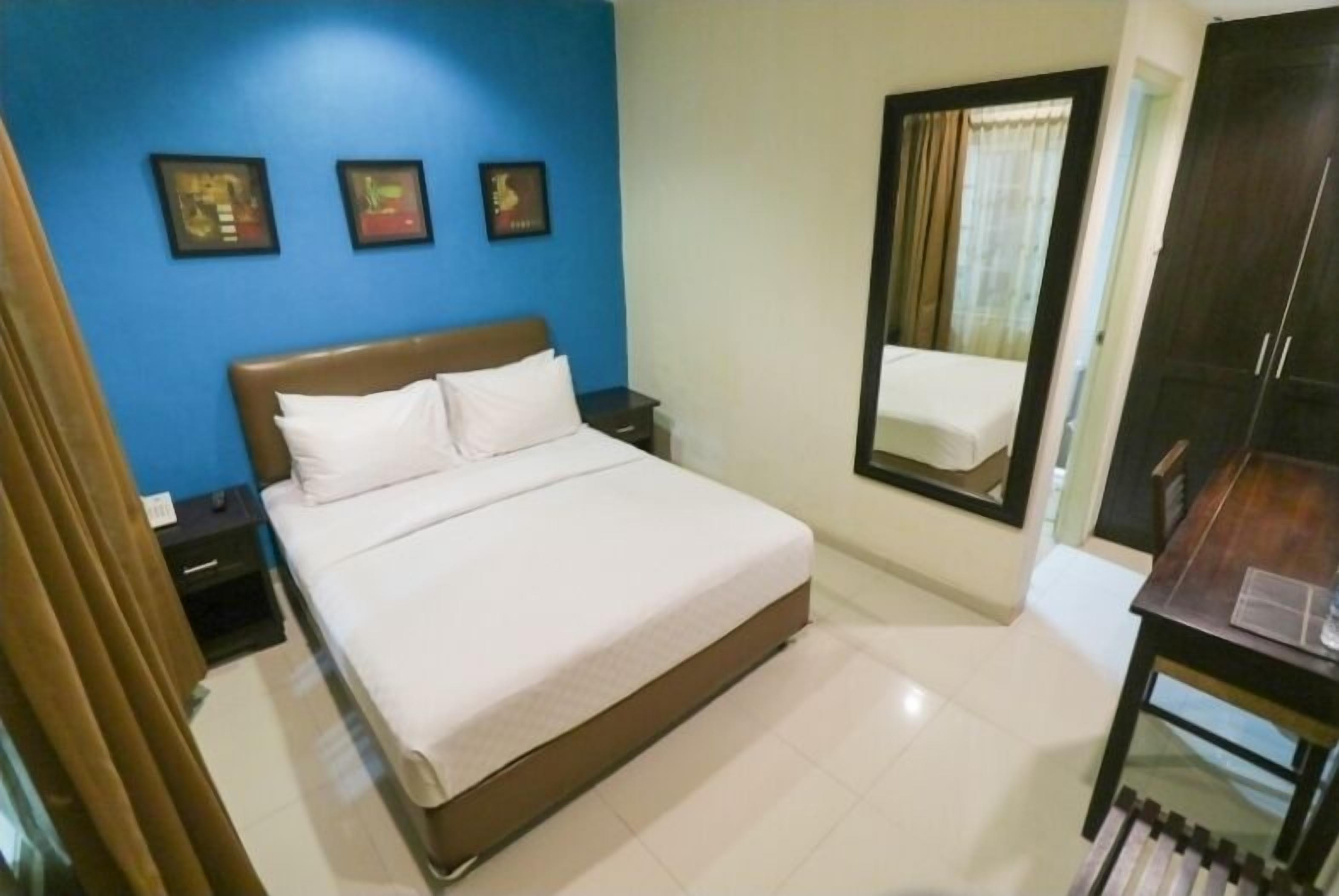 A bedroom with a bed, a nightstand, a dresser, and a mirror.