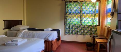 A hotel room with two beds, a small table, and a window with curtains.