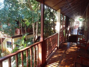 A covered outdoor area with a wooden railing, a tiled floor, and lush greenery. - Golden Triangle Palace (Chiang Rai)