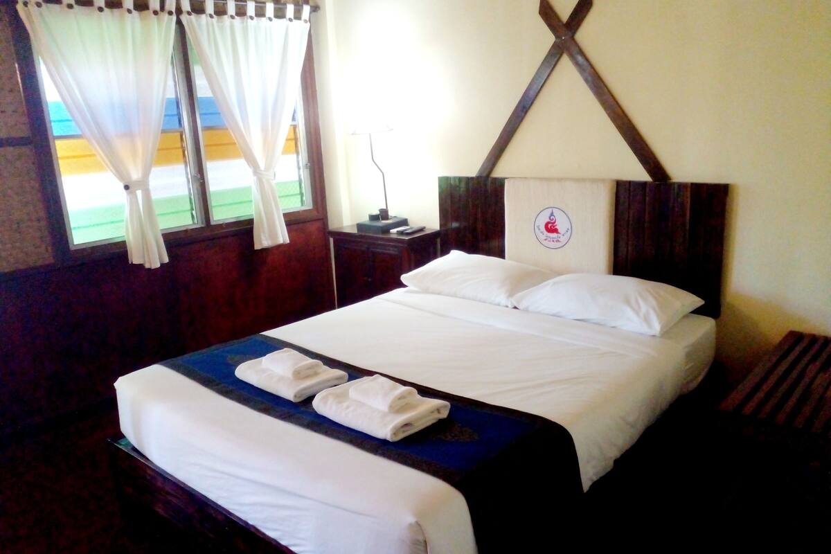 A hotel room with a neatly made bed, a nightstand with a lamp, and a window with curtains.