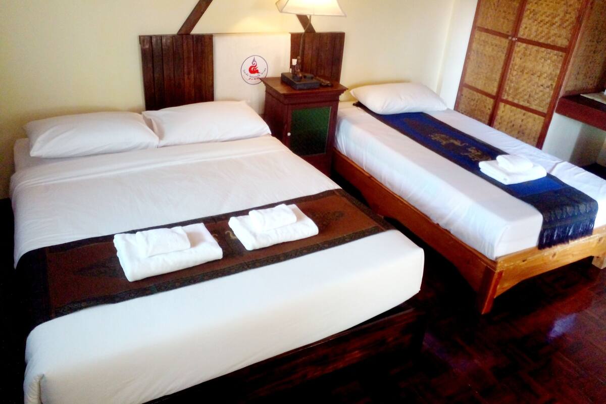 A hotel room with two beds, each with white linens and a wooden headboard. There is a nightstand with a lamp and a small table with a remote control.