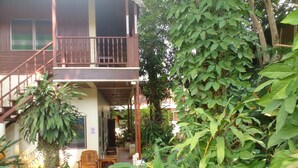 Une maison à deux étages dotée d’un balcon en bois, d’un escalier et d’un jardin agrémenté de différentes plantes.
