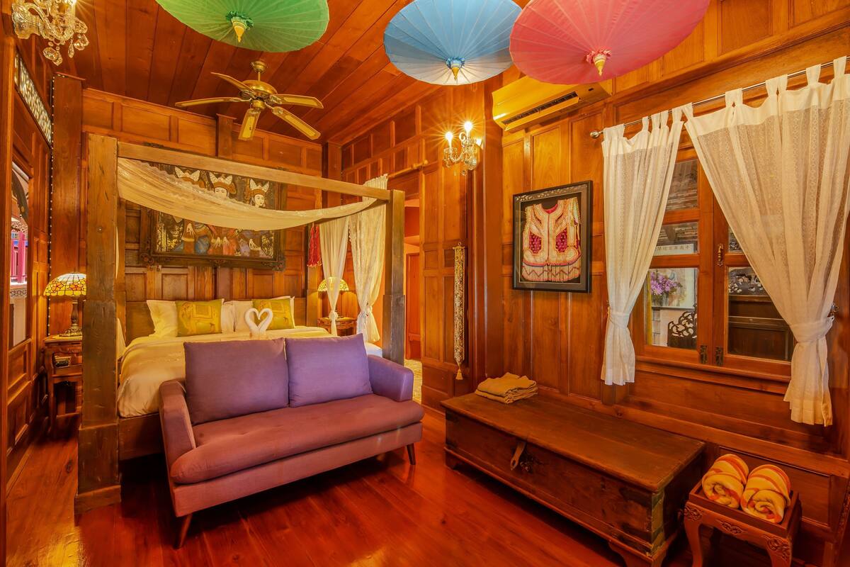 Une pièce en bois avec un lit, un canapé violet, un banc et un ventilateur de plafond.