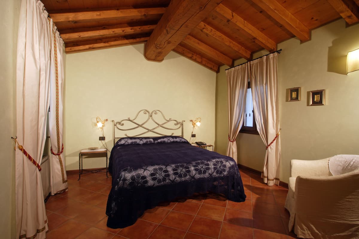A bedroom with a bed, a chair, a nightstand, and a window with curtains.