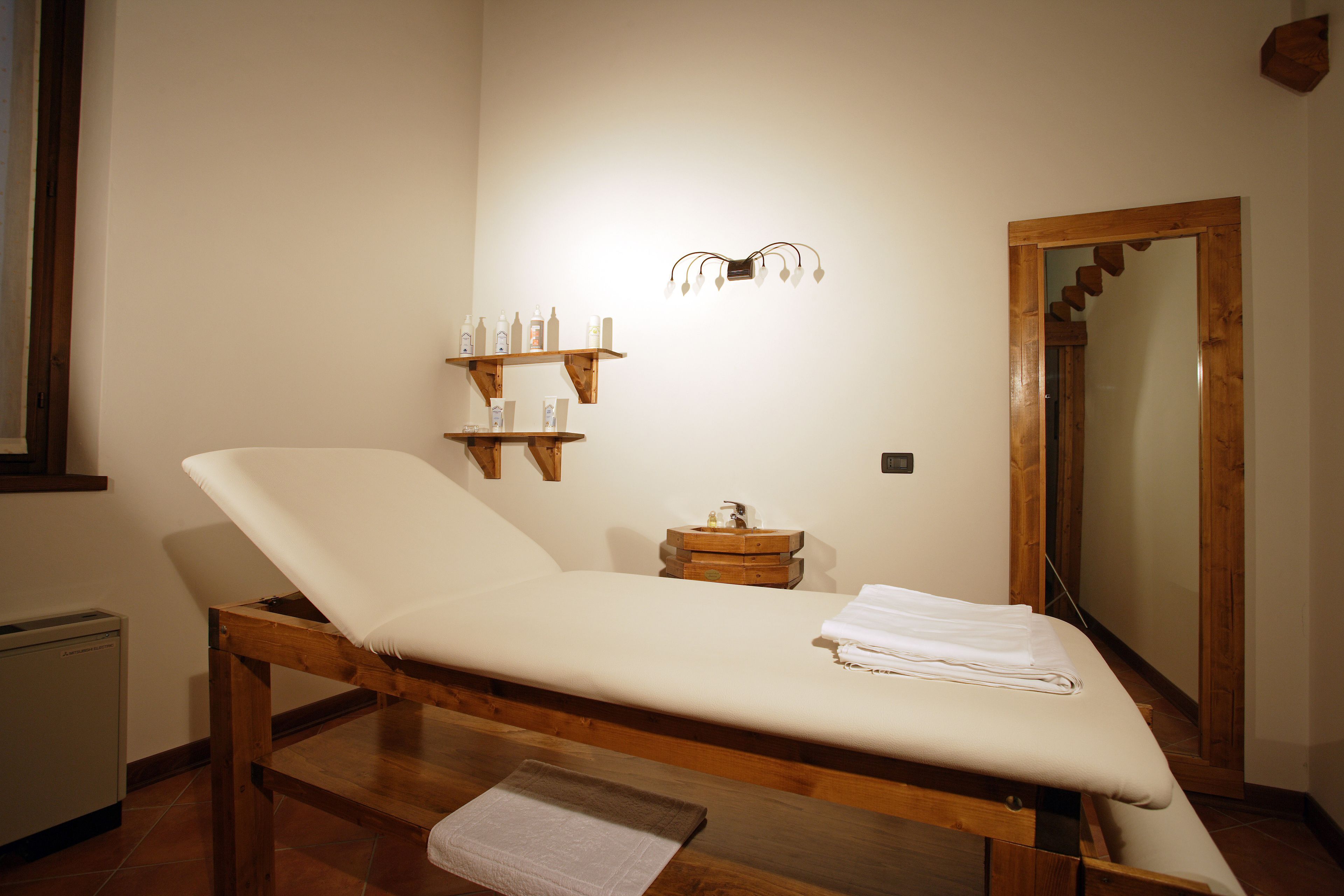 A room with a wooden bed, a small bedside table, a wall-mounted shelf with toiletries, and a mirror.