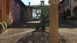 Un patio exterior con senderos adoquinados, un árbol y edificios con arcos y una torre de ladrillo.