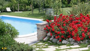 Una piscina rodeada por un jardín con flores rojas y un muro de piedra.