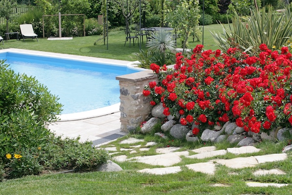 A swimming pool surrounded by a garden with red flowers and a stone wall. - Agriturismo Macesina (Bedizzole)