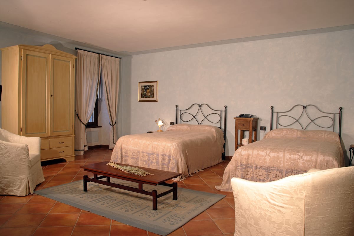 A bedroom with two beds, a wooden wardrobe, a bedside table, and a small table with a lamp.