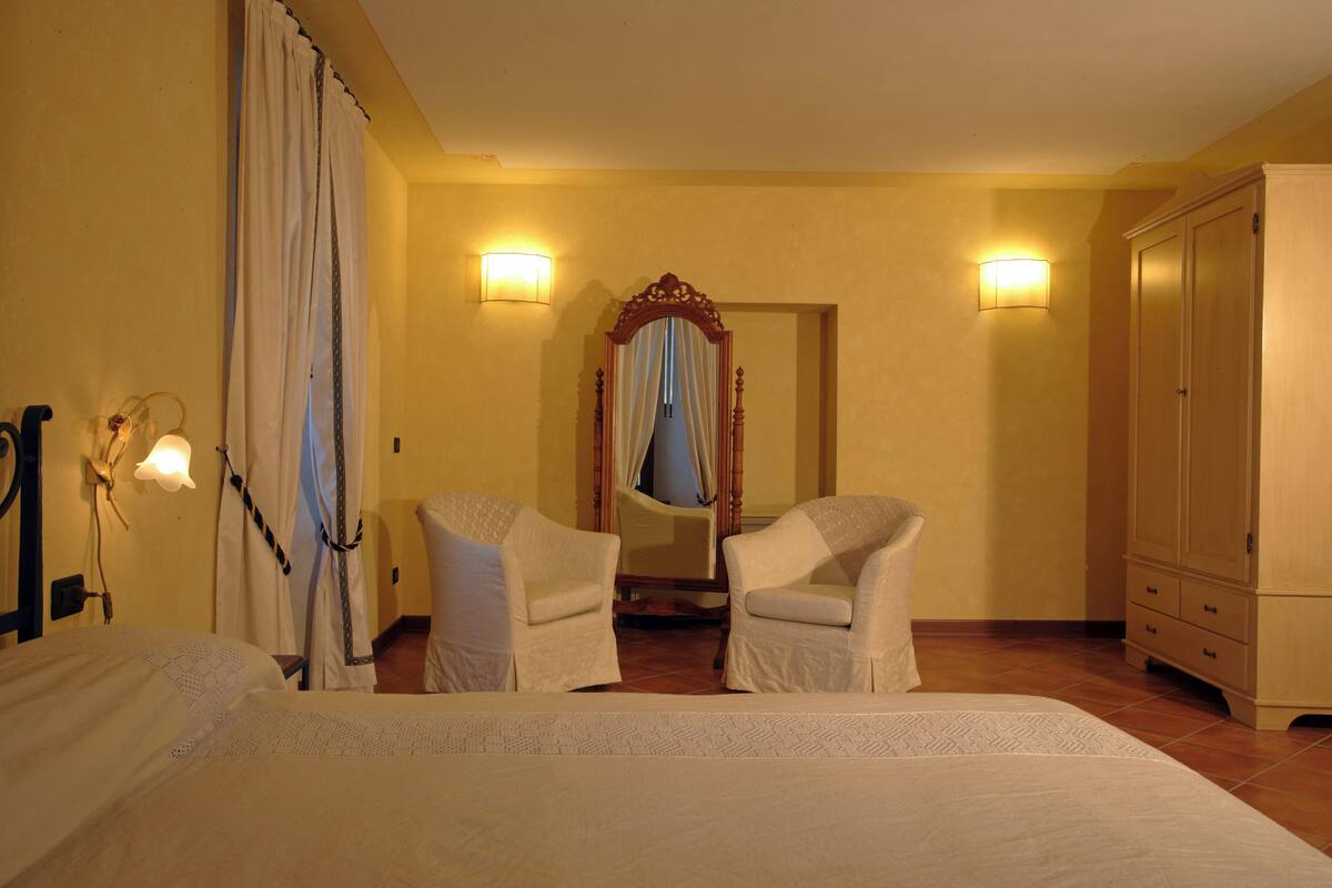 A hotel room with two beds, a mirror, two chairs, a wardrobe, and two wall-mounted lamps.