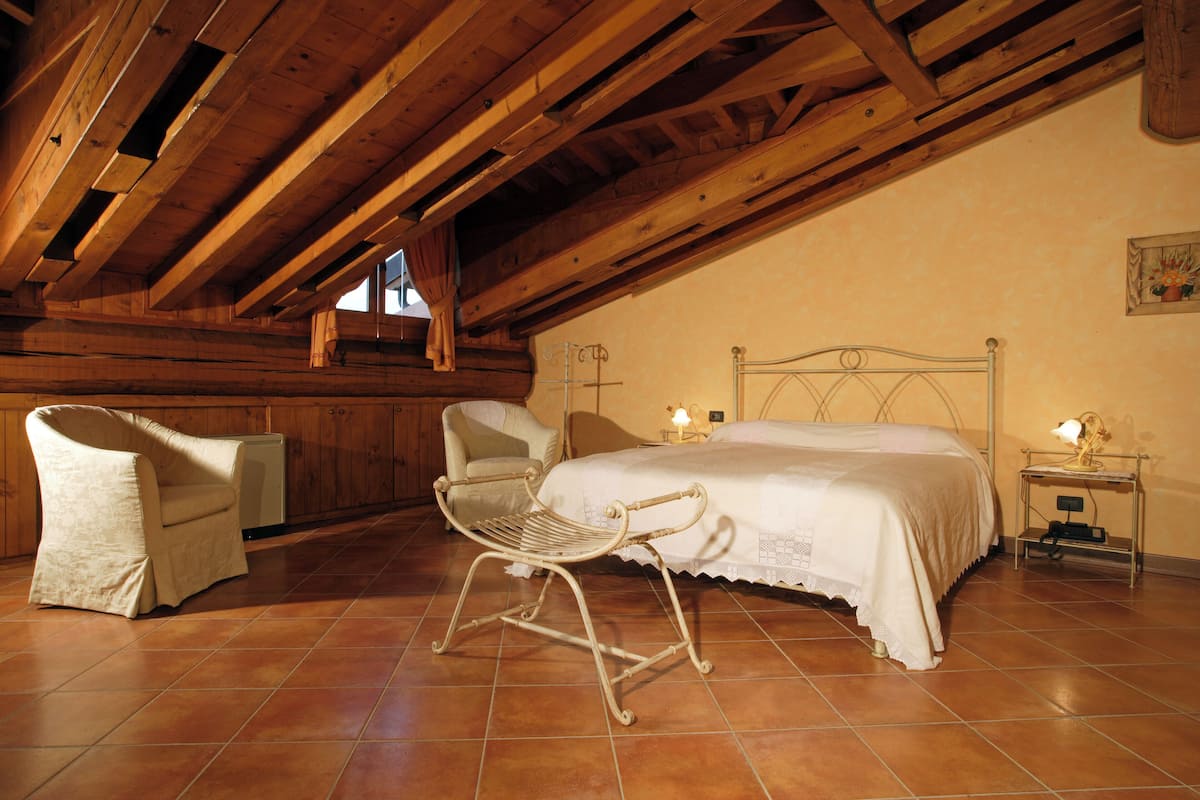 A bedroom with a wooden ceiling, a bed, a chair, a bedside table, and a lamp.